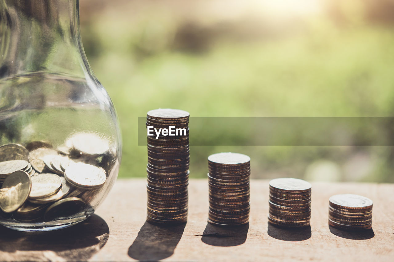 Close-up of coins stacks by jar on table