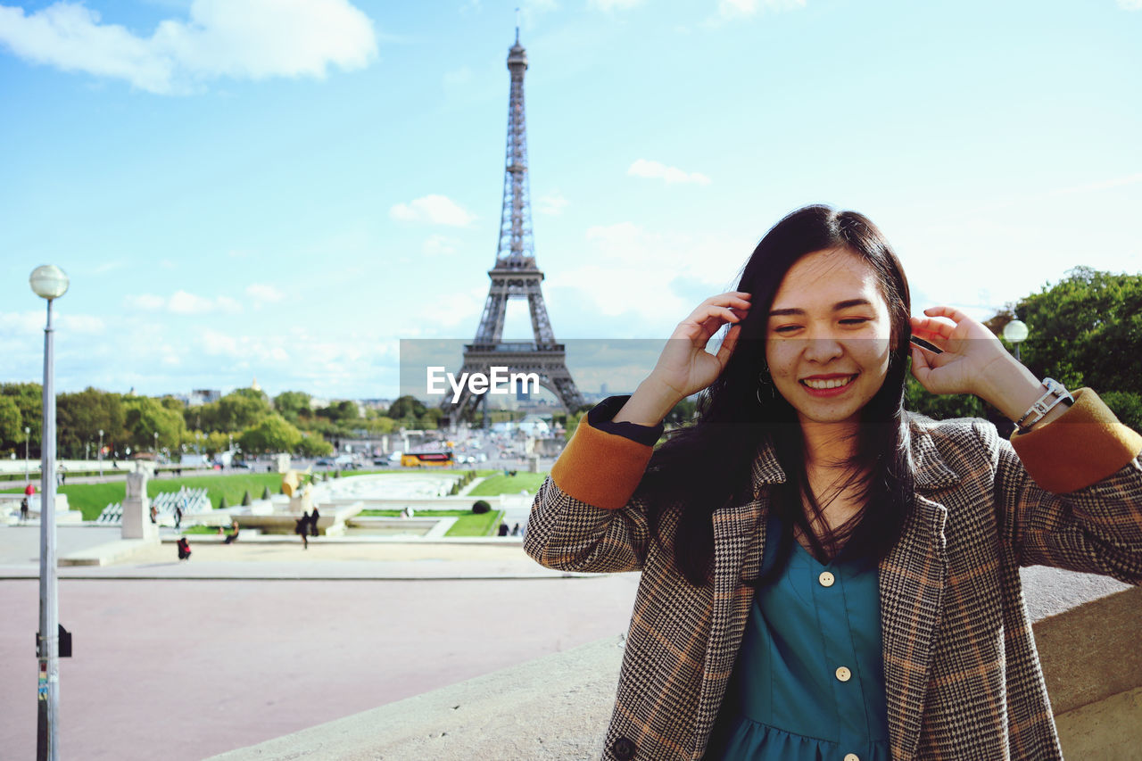 Young woman with hand in hair standing against eiffel tower