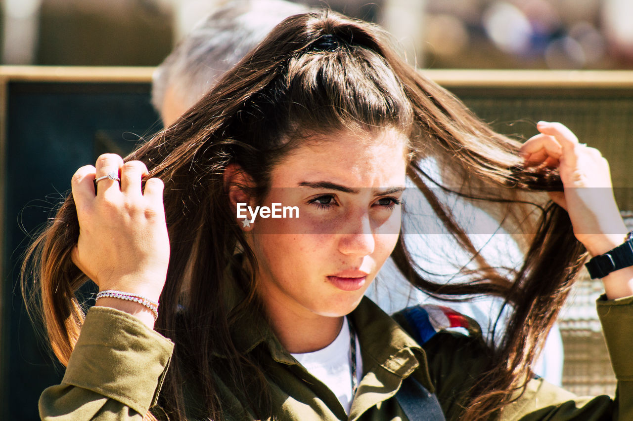 CLOSE-UP PORTRAIT OF YOUNG WOMAN WITH HANDS HOLDING HAIR