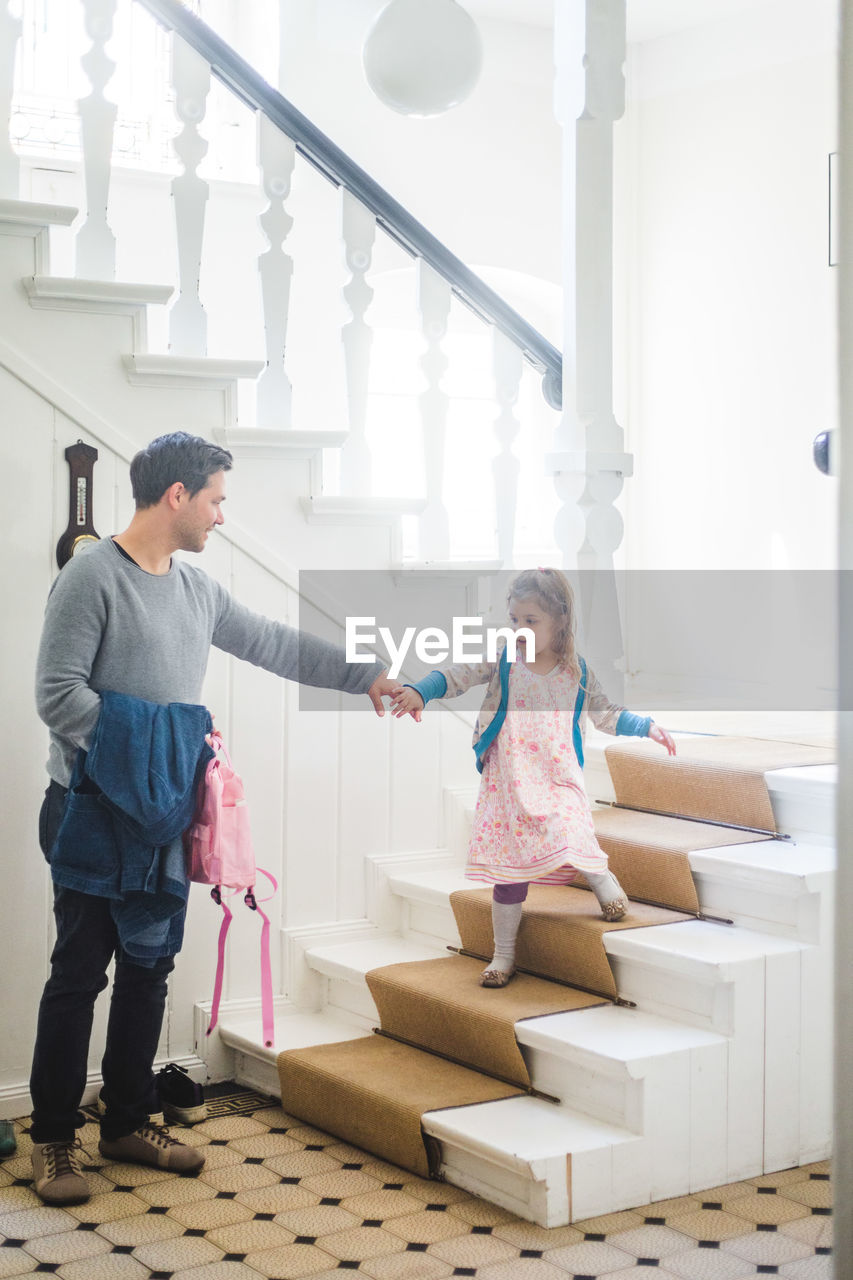 Full length of father holding schoolgirl moving down steps at home