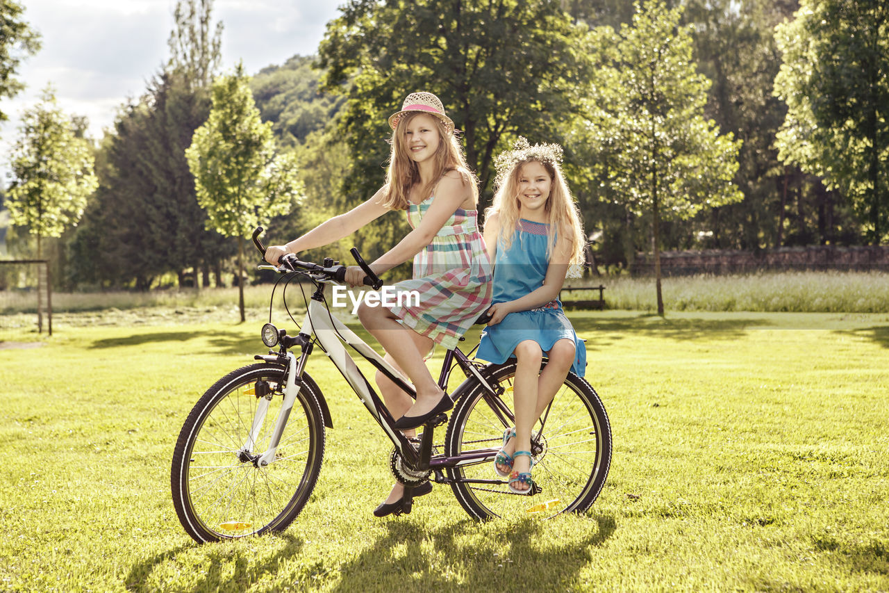 Woman and girl riding bicycle on grass against trees