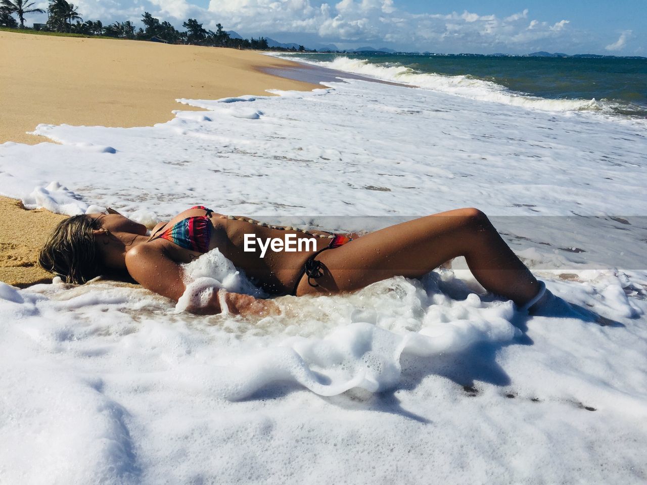 Full length of young woman wearing bikini while lying at shore