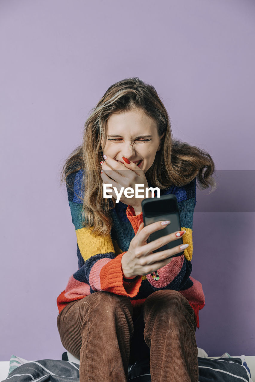 Smiling girl using smart phone sitting against purple background