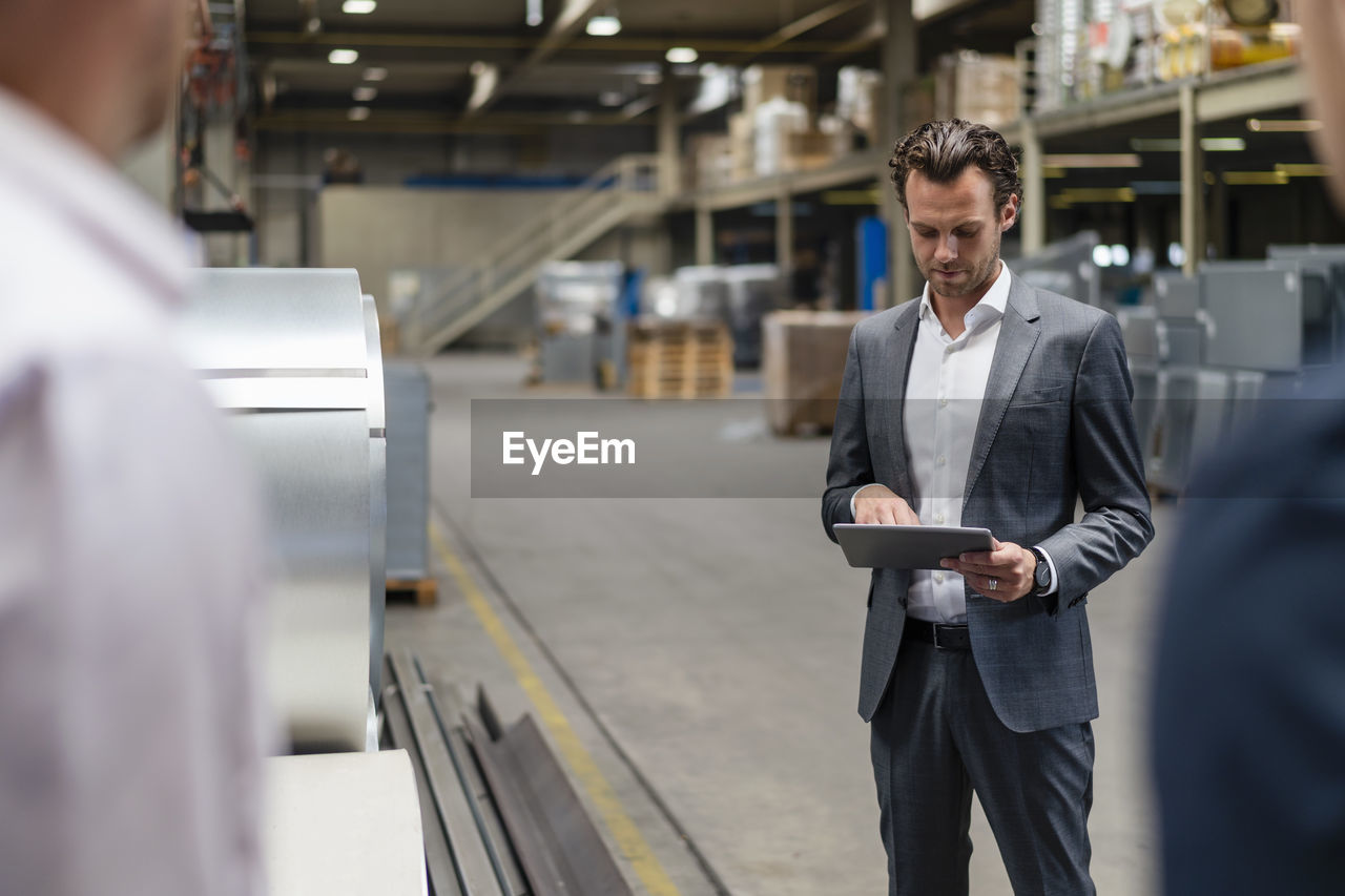 Businessman using digital tablet while standing near colleagues in factory