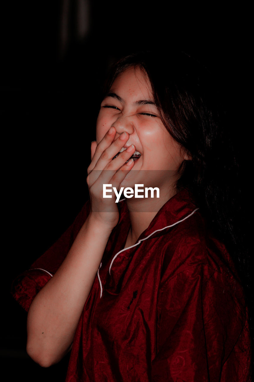 Beautiful young woman with eyes closed laughing while hands covering mouth