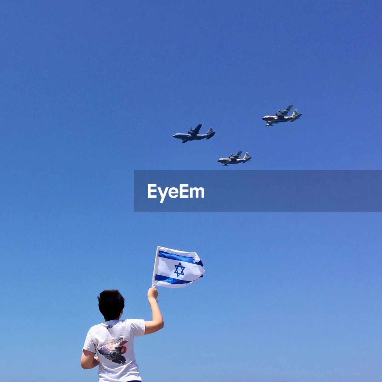 Low angle view of boy with israeli flag looking at airplane against sky