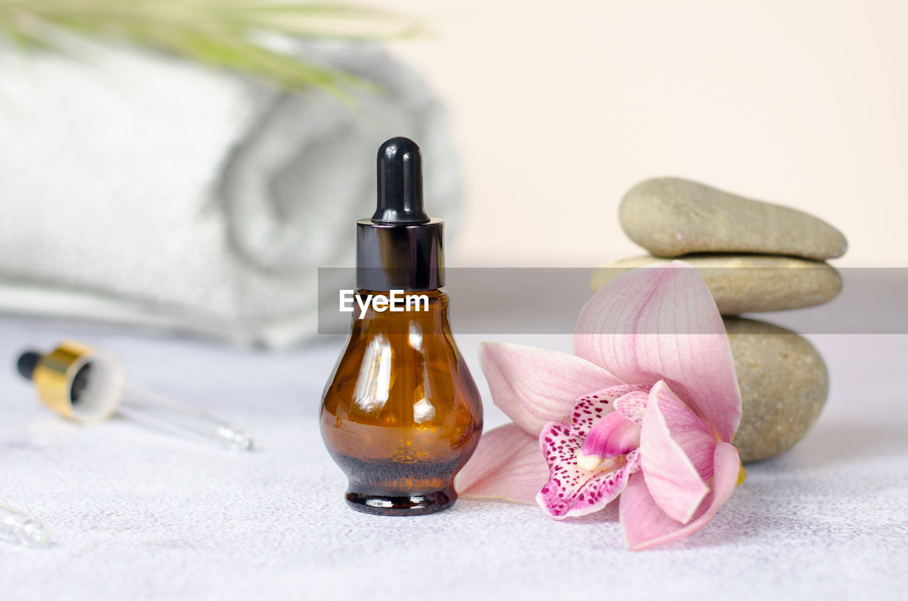 Composition of natural stones, orchid flower, rolled white towel and bottle of essential oil.