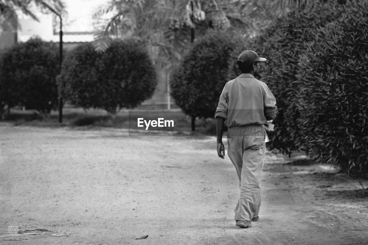 FULL LENGTH REAR VIEW OF MAN WALKING ON ROAD