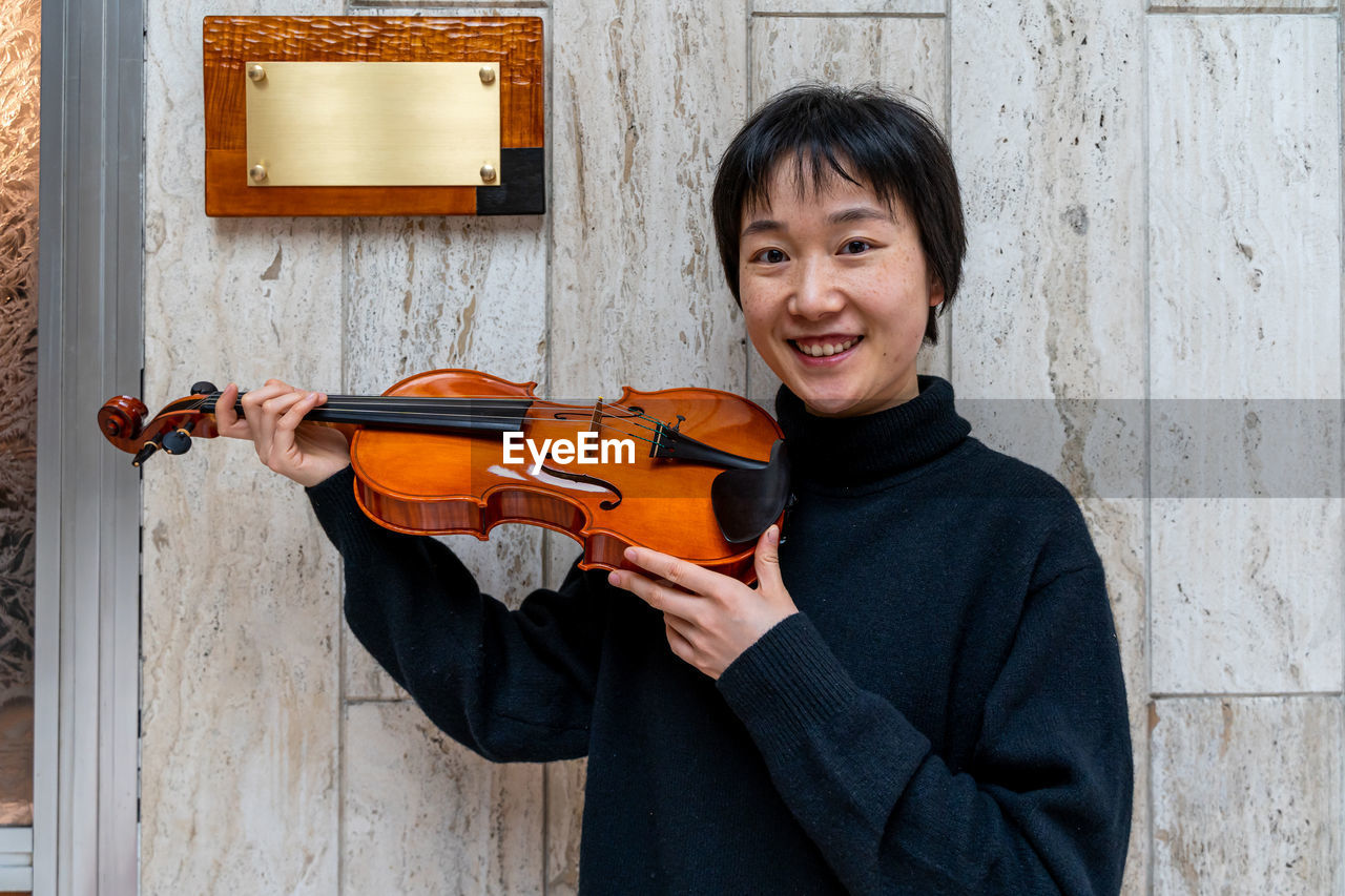 Young chinese female violin maker showing her freshly made violin outdoors in front of her workshop