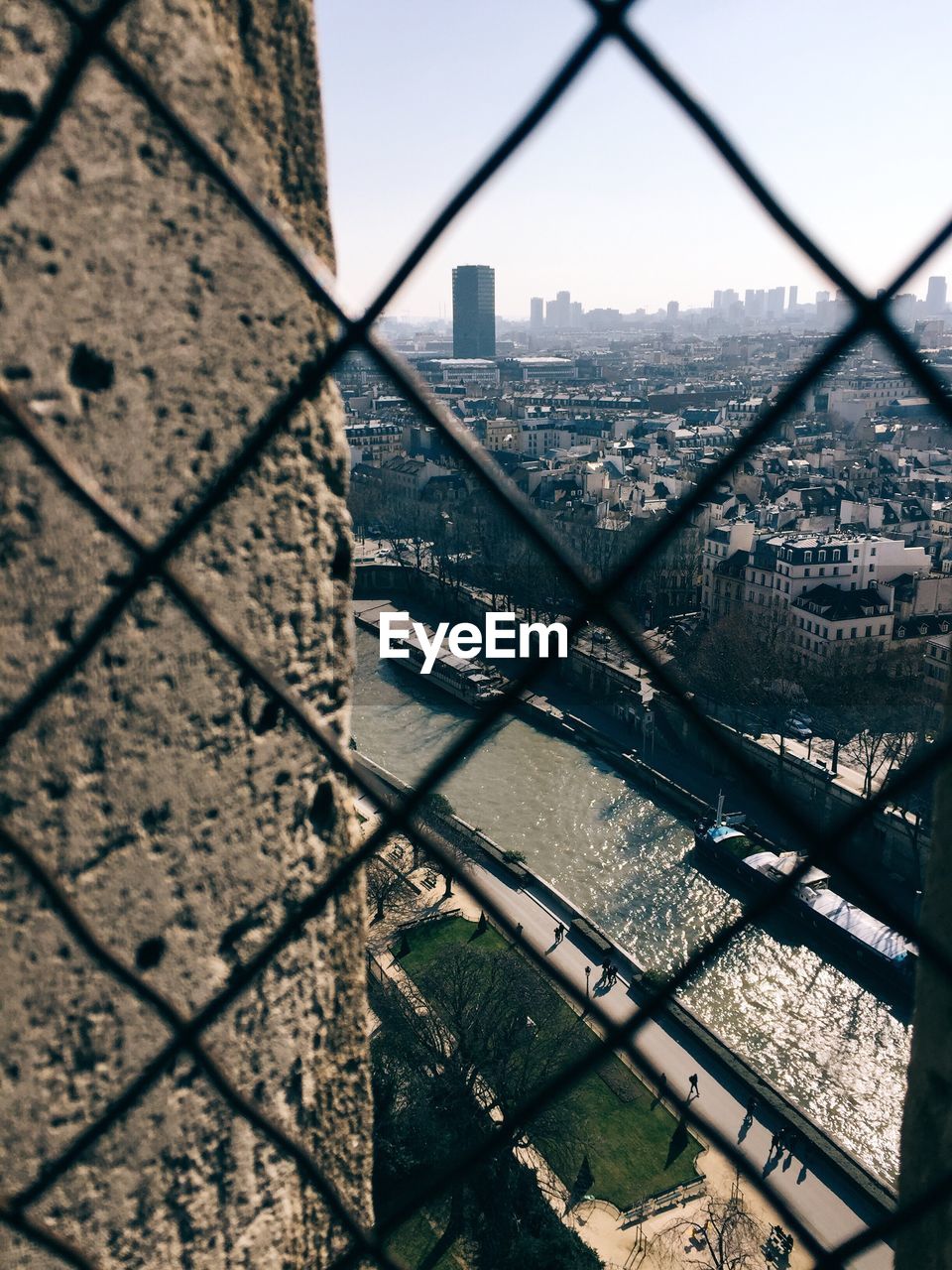 Seine river amidst cityscape against sky seen through chainlink fence