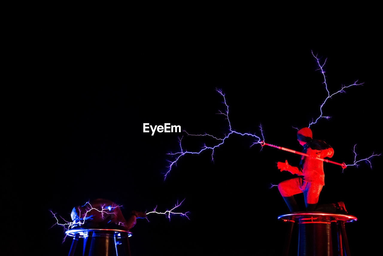 LOW ANGLE VIEW OF ILLUMINATED LIGHTS AGAINST BLACK SKY