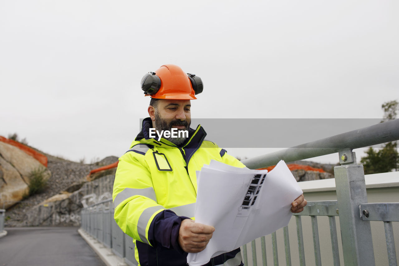 Male engineer in reflecting clothing looking at blueprint