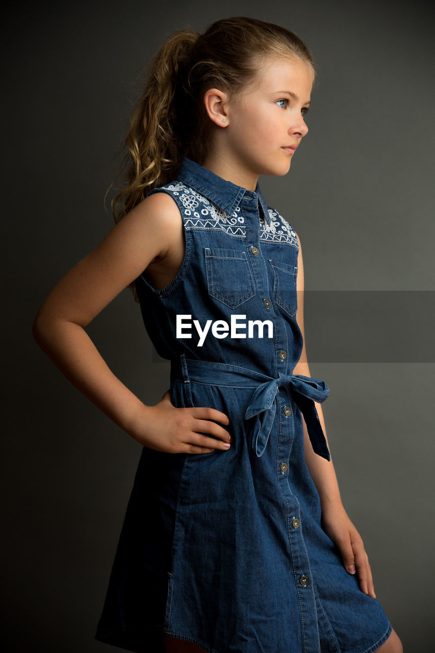 Girl with hand on hip looking away against gray background