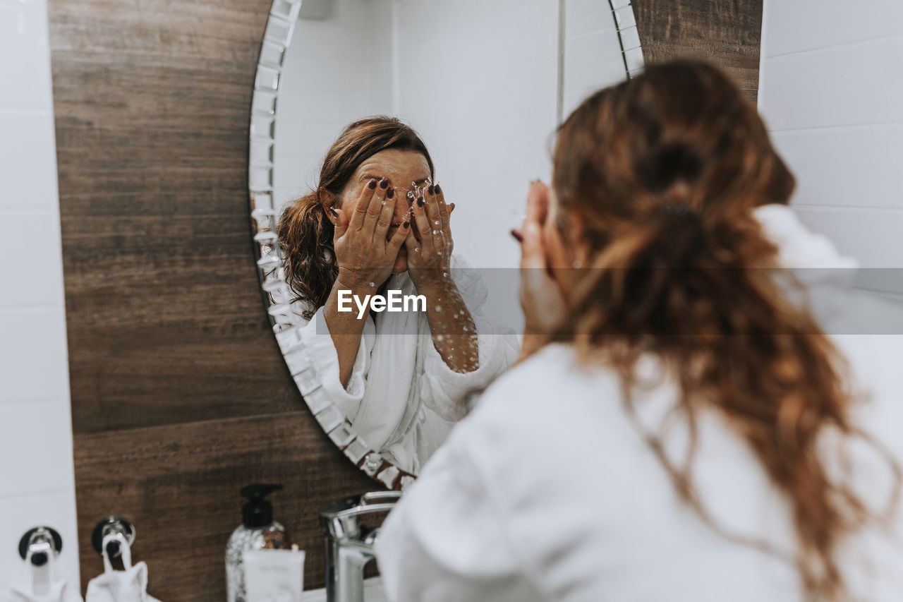 Woman washing her face in front of mirror