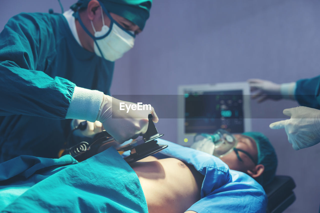 While performing medical surgery inside the operating room, a doctor and nurse use a defibrillator.