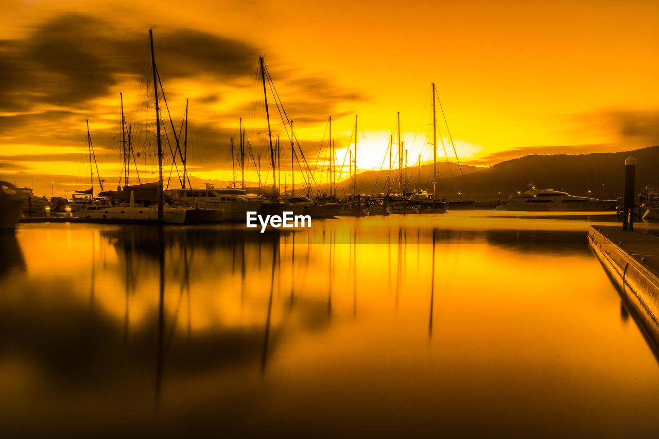 Boats moored at harbor against orange sky