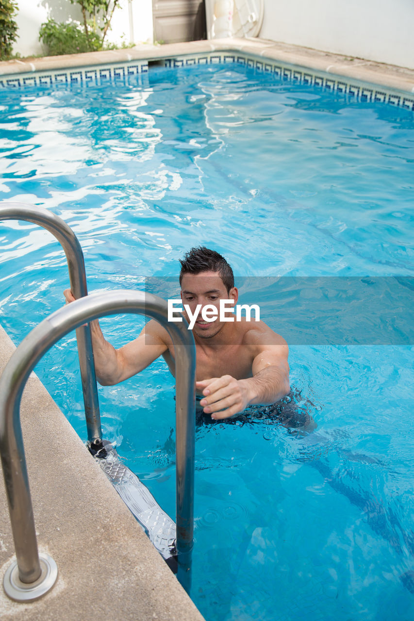 HIGH ANGLE VIEW OF SHIRTLESS MAN SWIMMING POOL