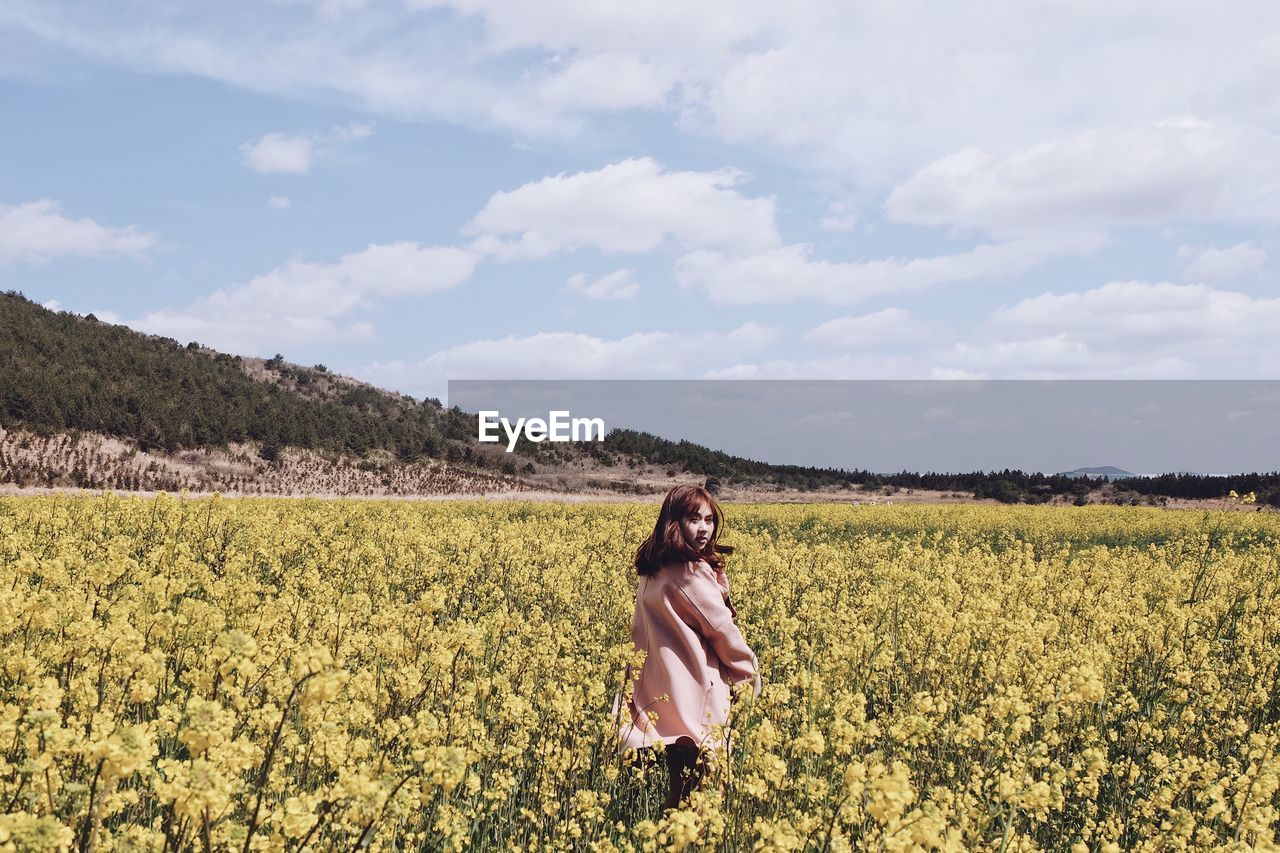 Portrait of woman standing amidst flowering plants against sky