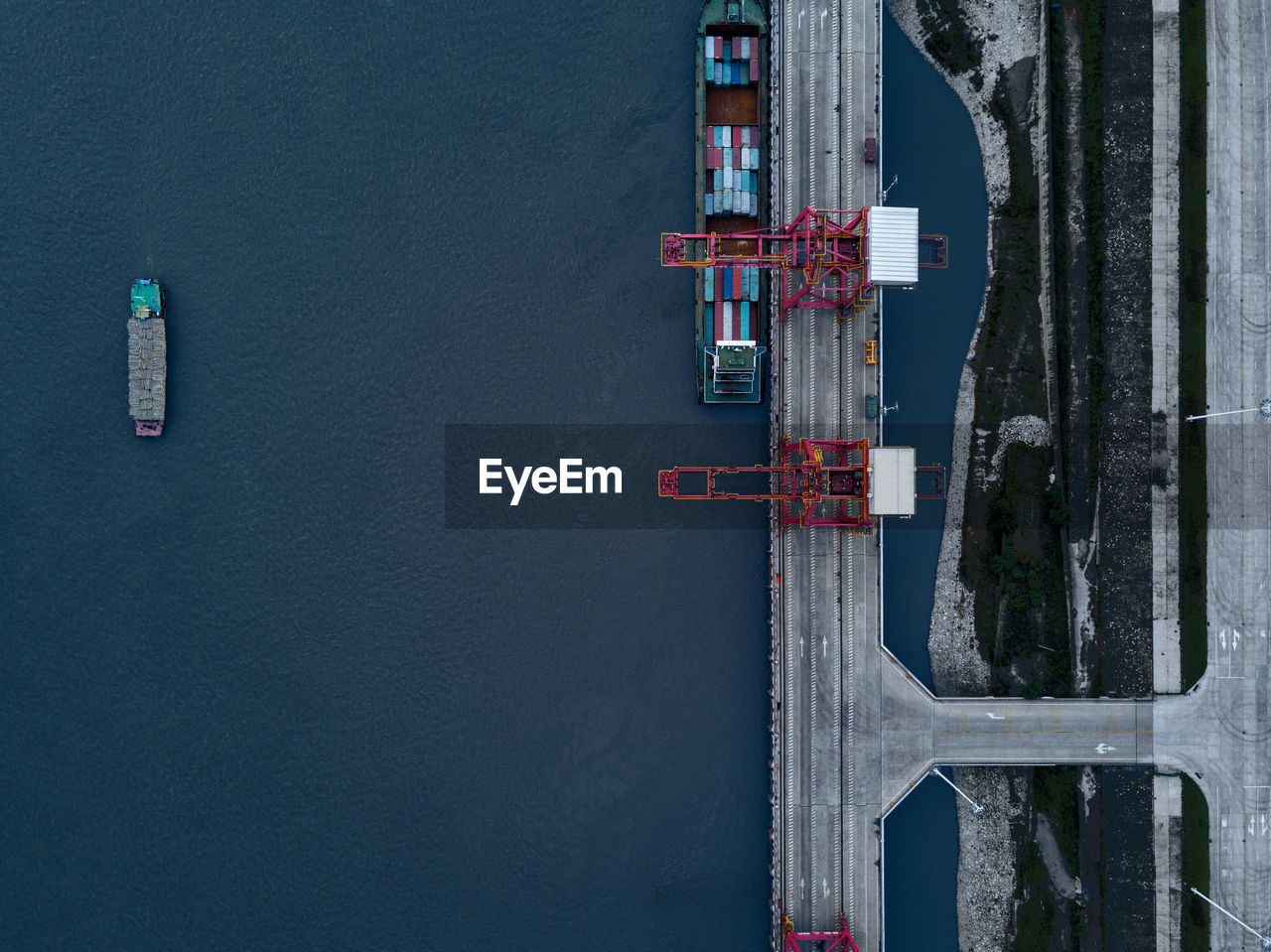 Aerial view of cranes on bridge by cargo ship over sea