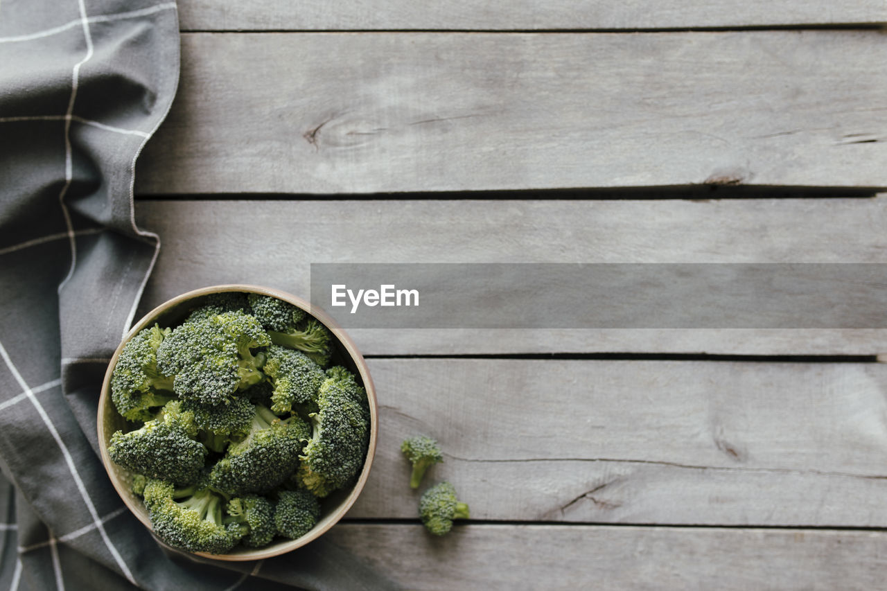 Green fresh broccoli in bowl on wooden background, gray towel. healthy eating concept