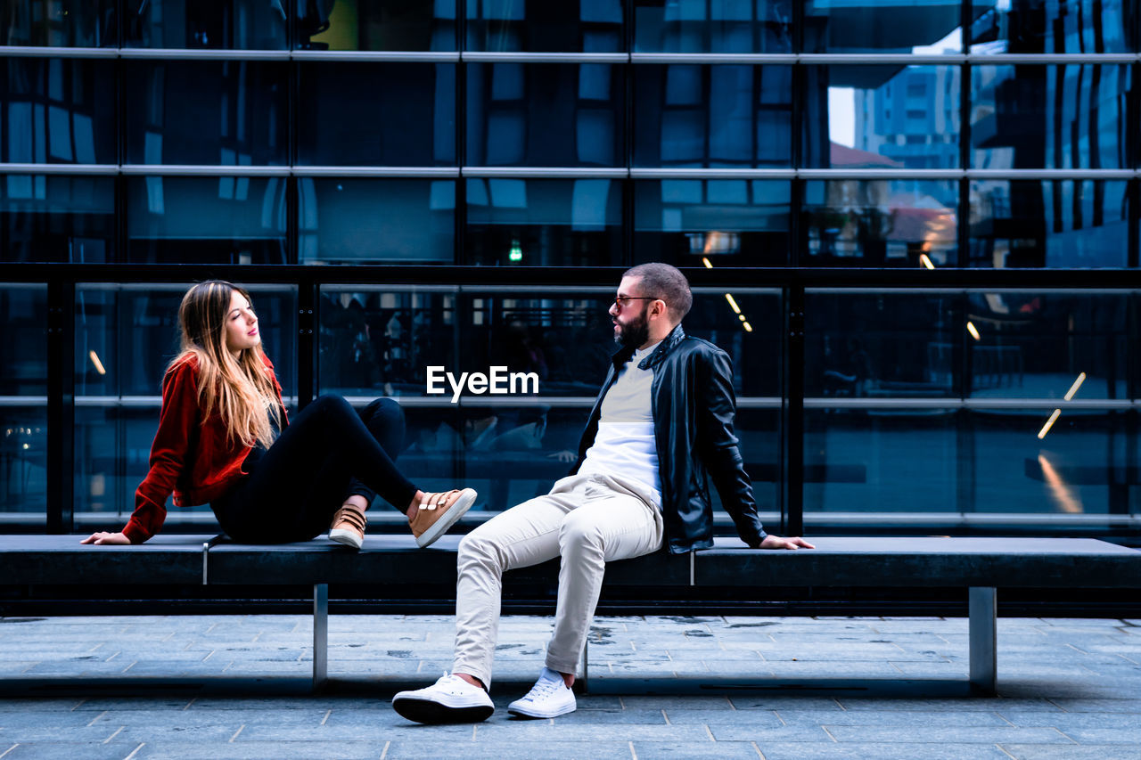 Man and woman sitting on seat against building in city