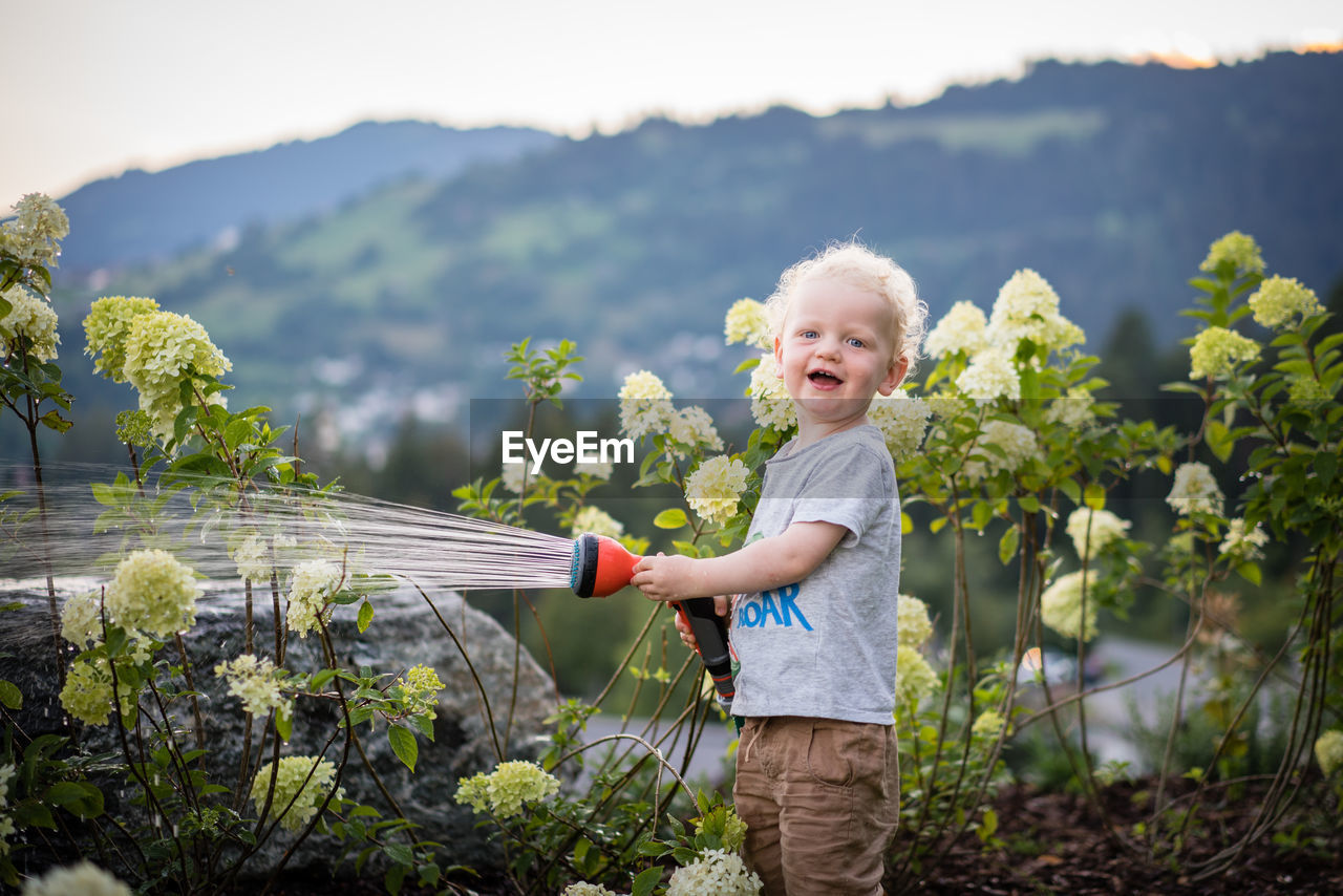 A boy laughing and watering flowers