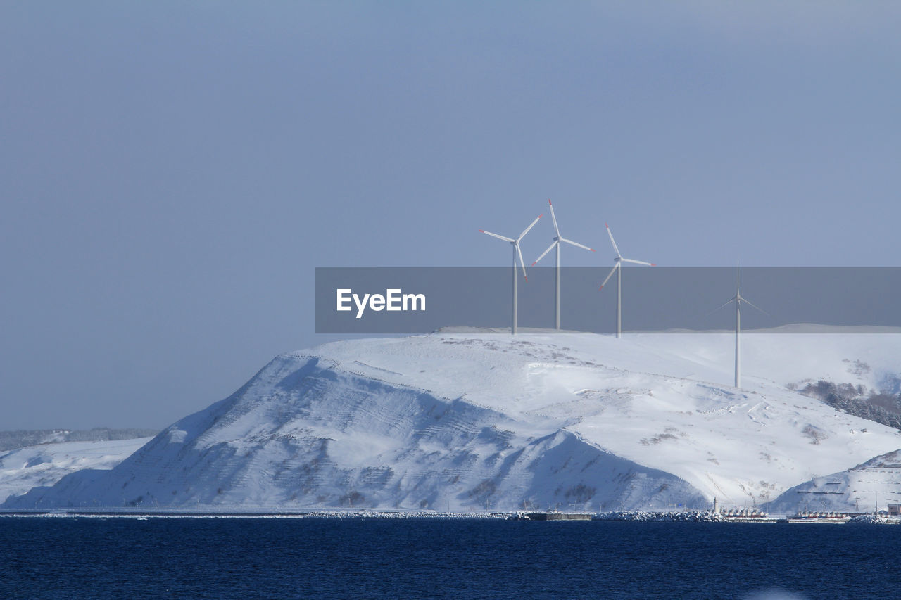 Scenic view of snowcapped mountains with wind turbines against sky