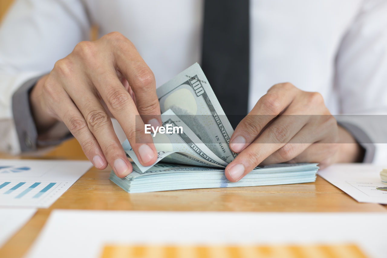 Midsection of businessman counting paper currency on desk