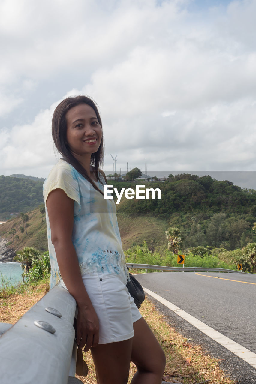 PORTRAIT OF WOMAN STANDING ON ROAD AGAINST SKY