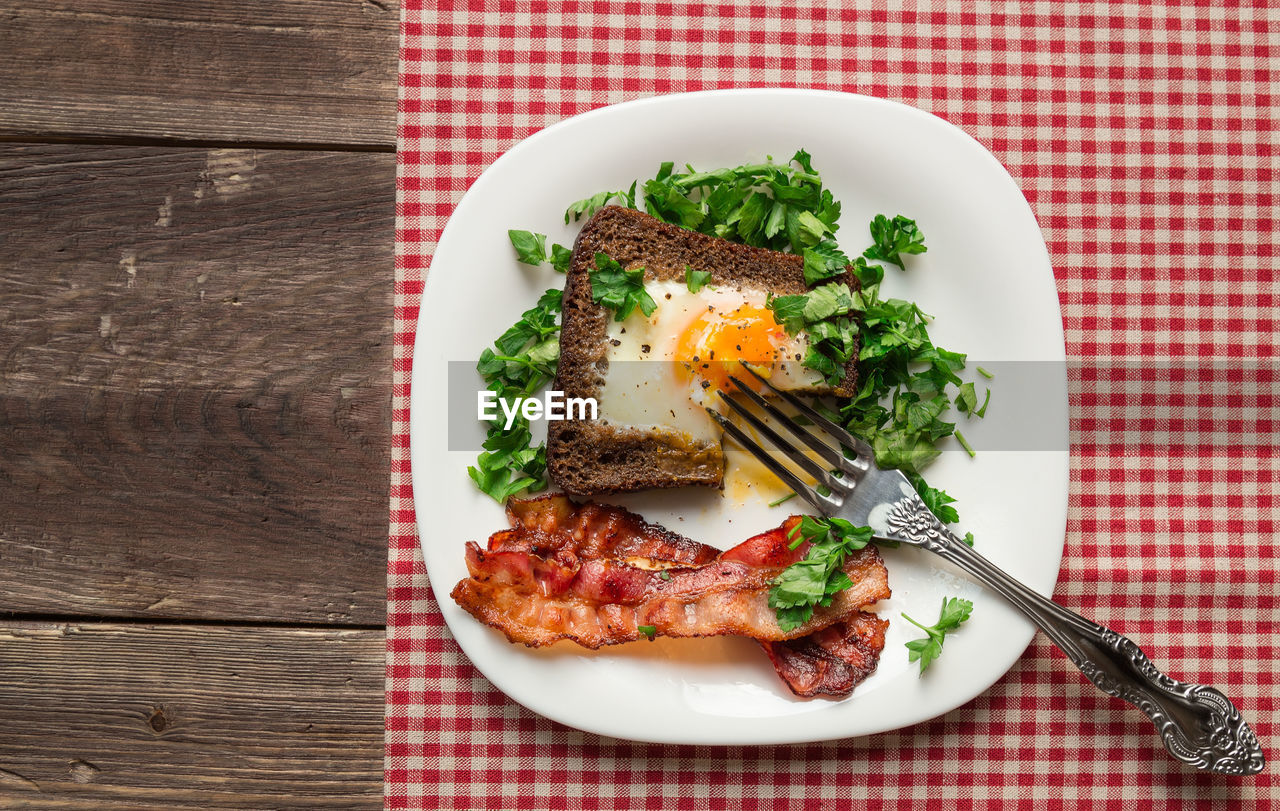 Fried egg in rye bread with bacon and parsley on rustic wooden background. top view.