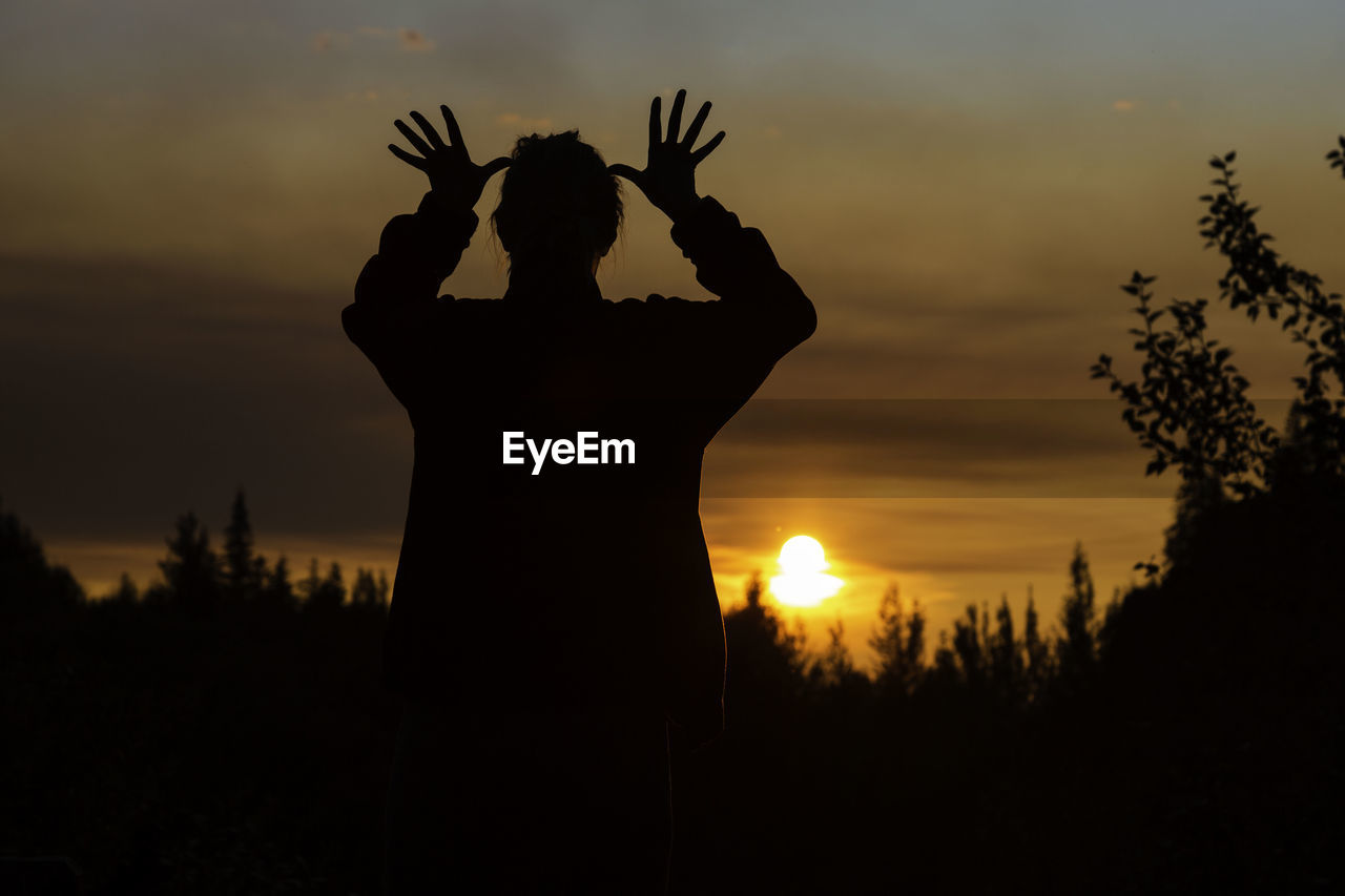 Silhouette woman with arms raised standing against sky during sunset