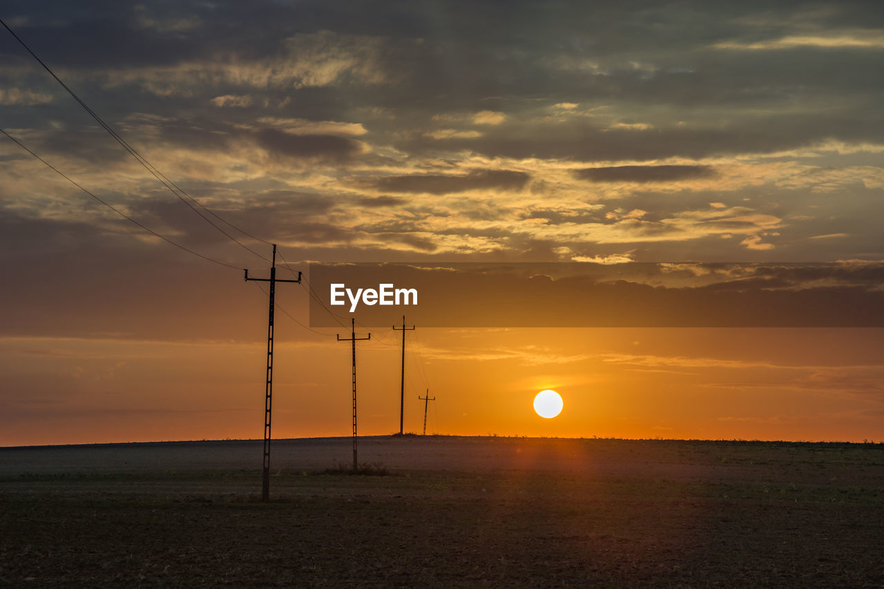 Sunset behind the horizon and electric poles in the field