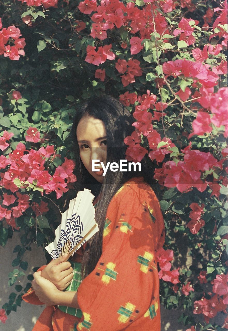 YOUNG WOMAN WITH PINK FLOWER STANDING BY PLANTS