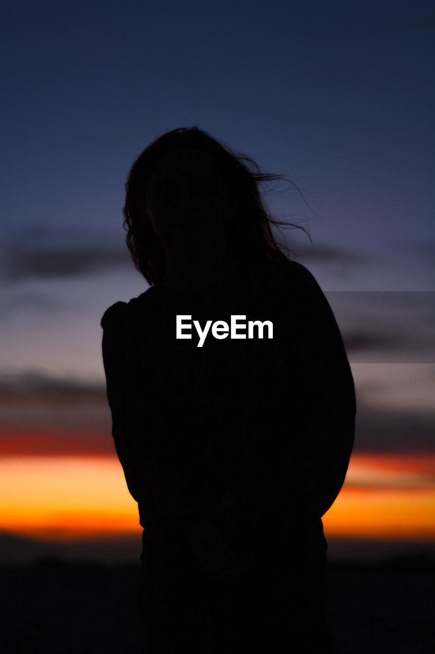 Rear view of silhouette woman standing against sky during sunset