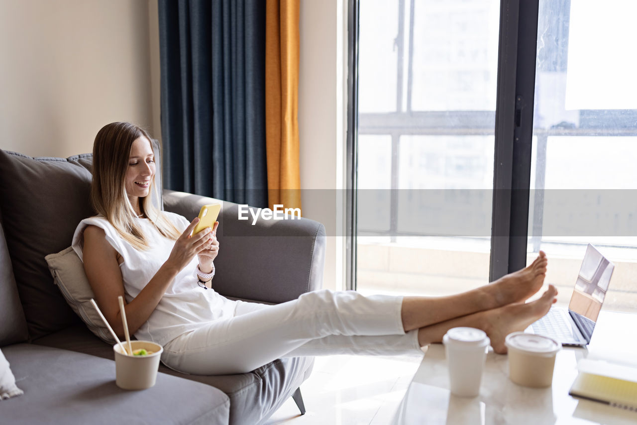 Full length of woman using mobile phone while sitting on sofa