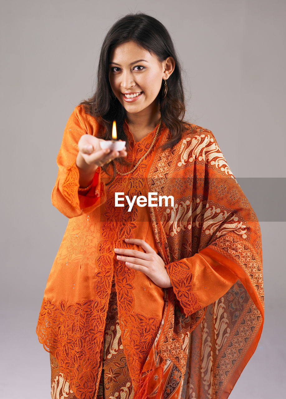 Portrait of smiling woman holding diya against gray background