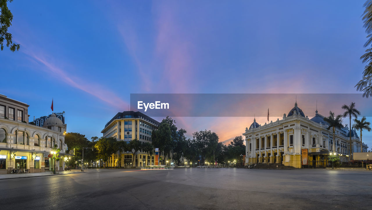 Street by buildings against sky at sunset