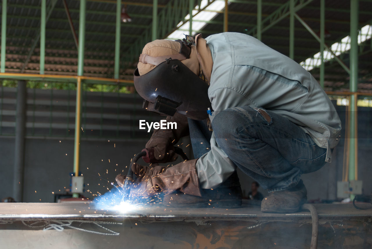 REAR VIEW OF MAN WORKING AT INDUSTRY