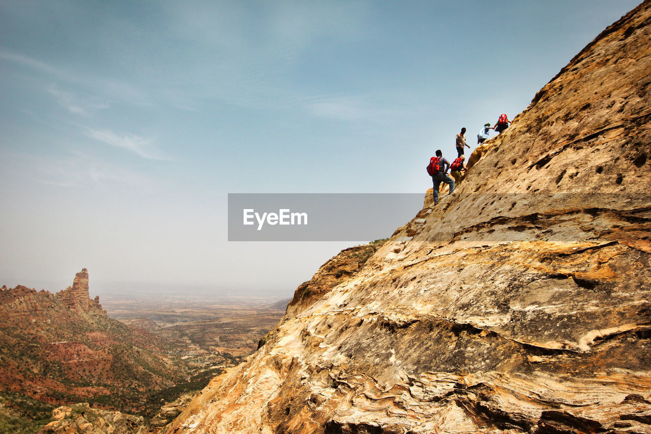 PEOPLE ON ROCKS AGAINST MOUNTAIN RANGE