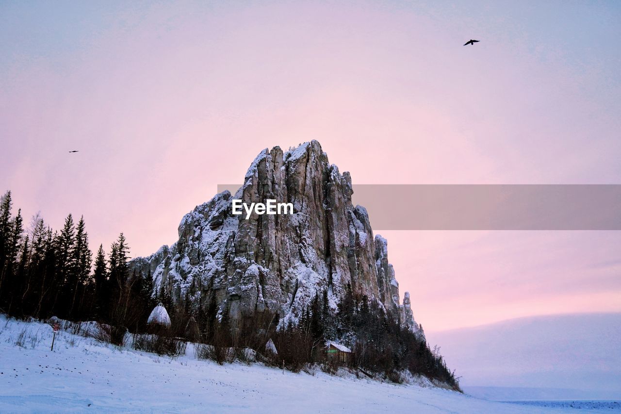 Low angle view of rock on snow covered landscape against sky at sunset