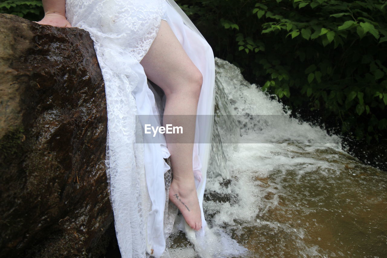 LOW SECTION OF WOMAN STANDING ON ROCK AT WATERFALL