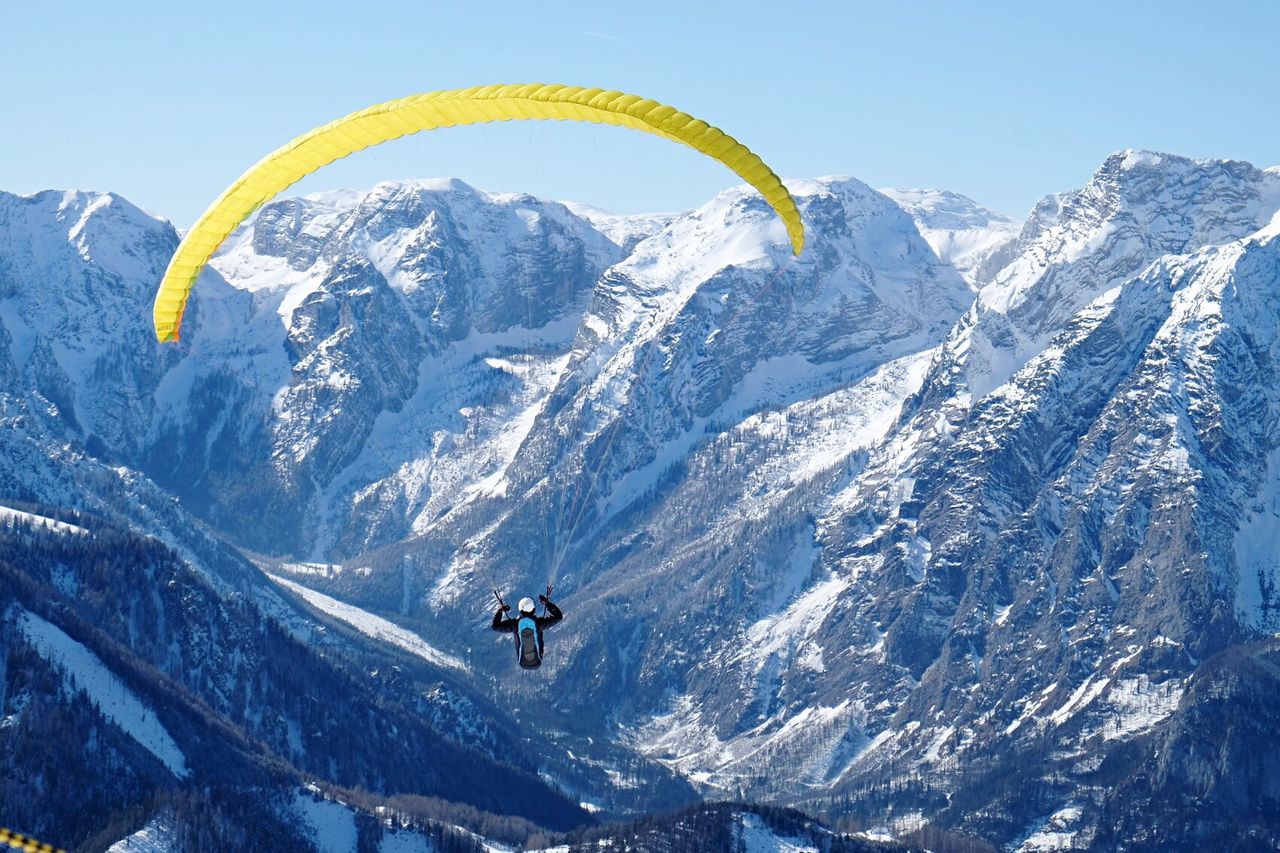 One person paragliding against snowcapped mountain and clear sky