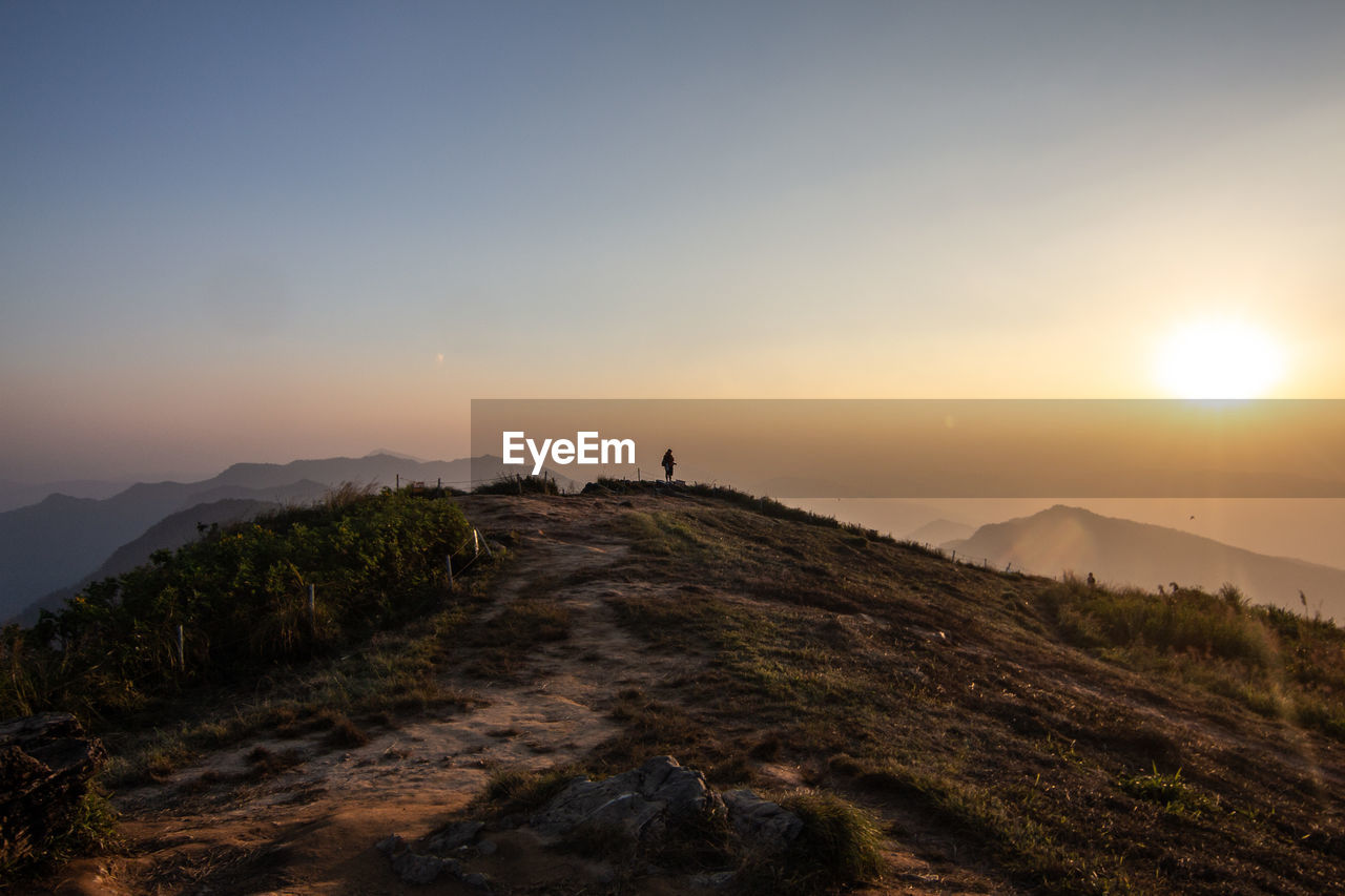 Mid distance view of person standing on mountain against sky during sunset