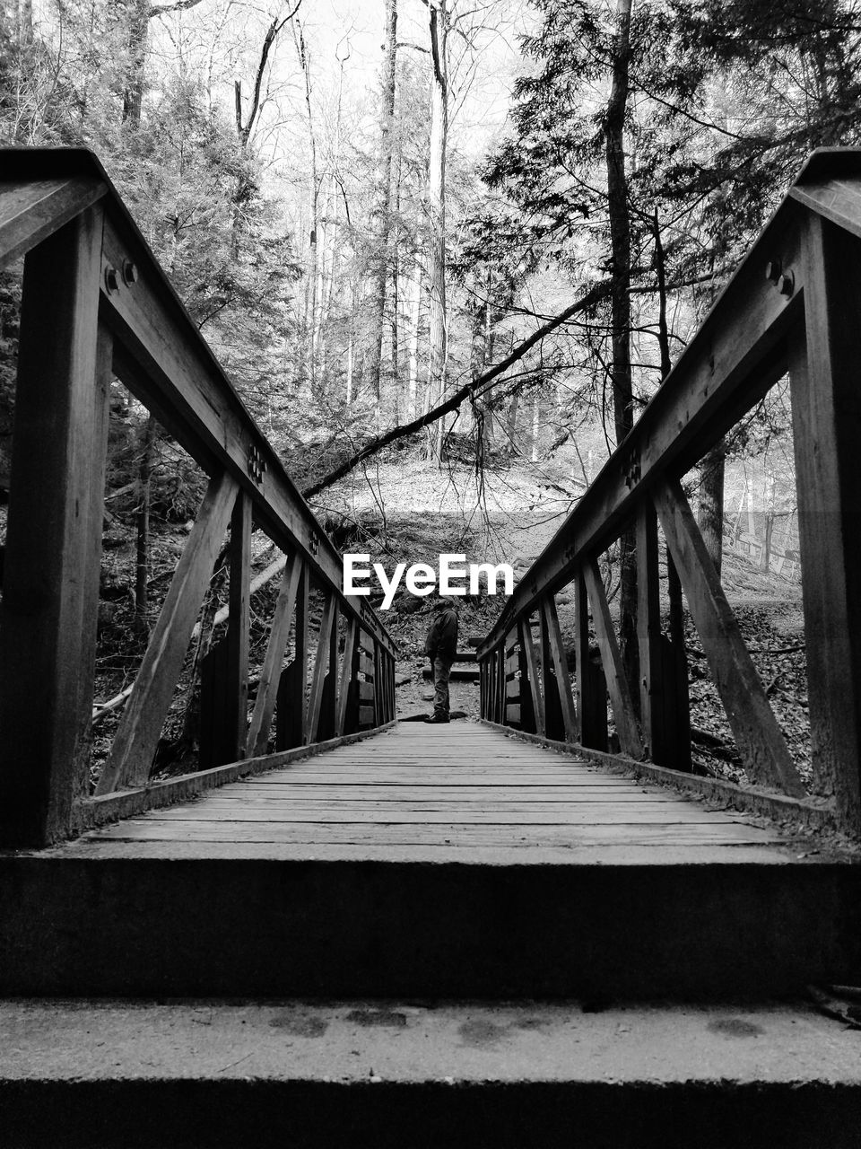 REAR VIEW OF MAN WALKING ON FOOTBRIDGE