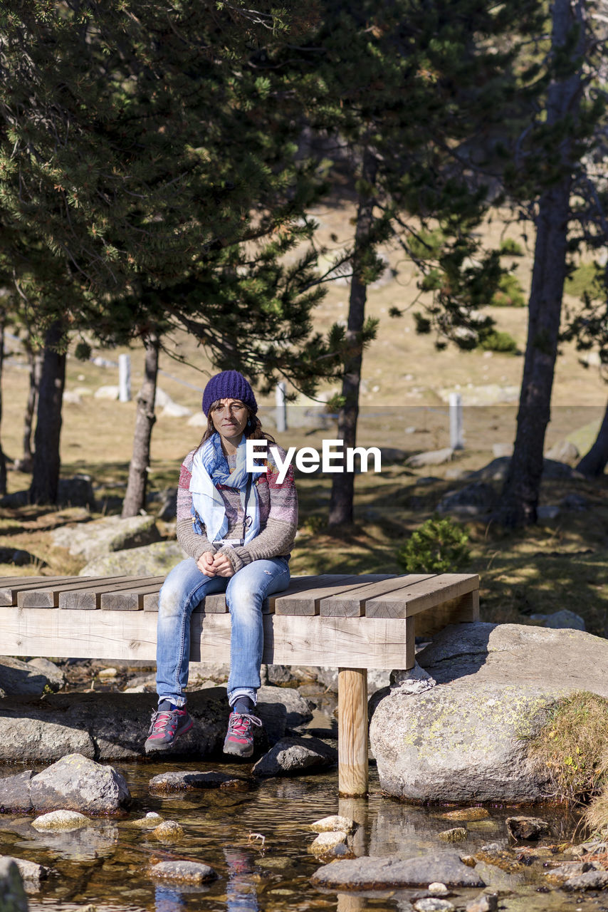 Full length of woman sitting on boardwalk against trees in forest