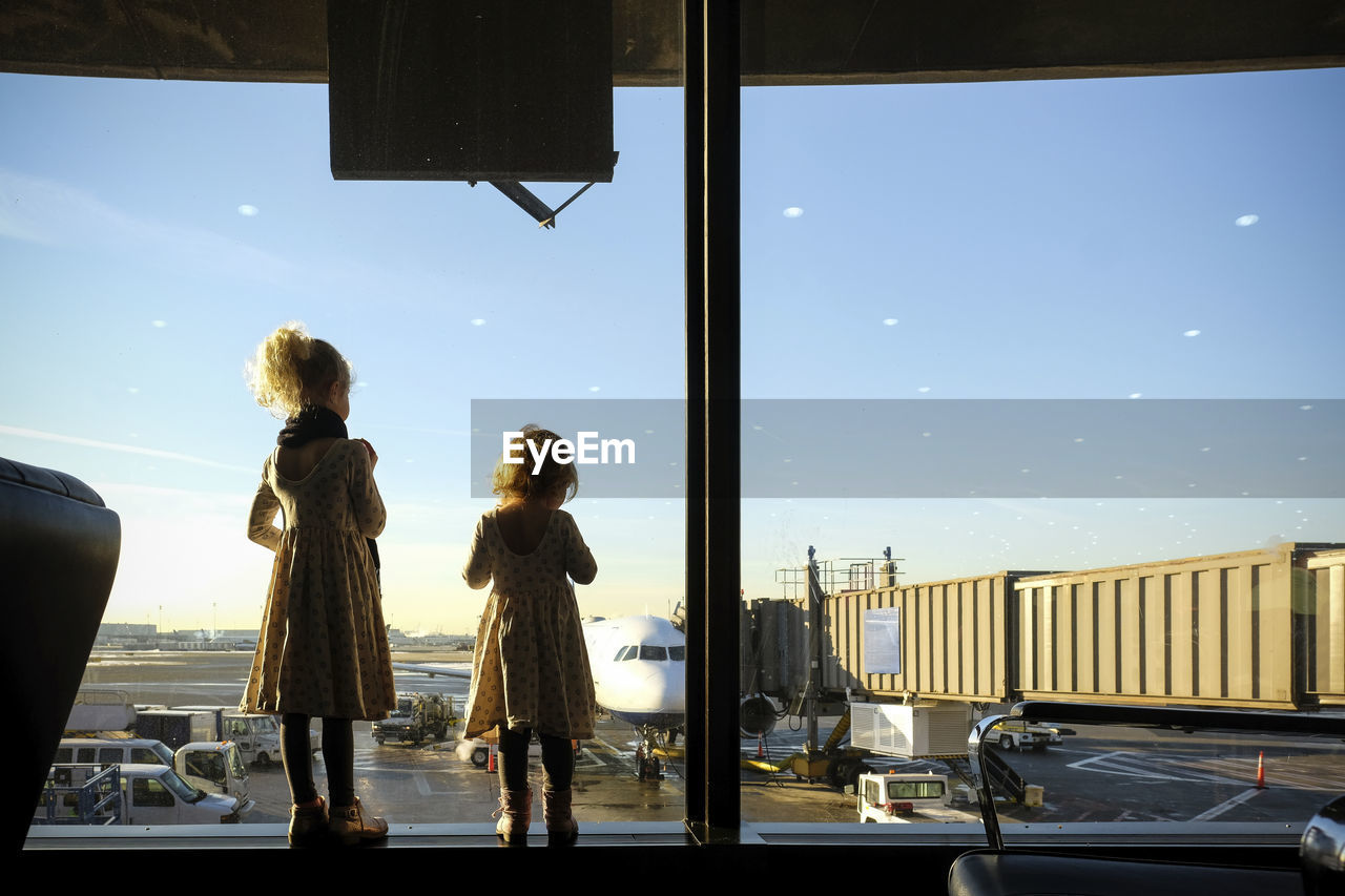 Rear view of sisters looking through window while standing at airport