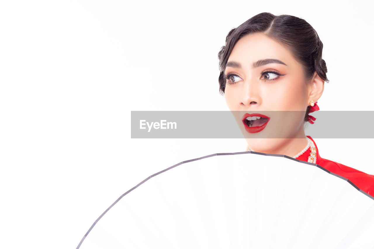 Woman looking away with hand fan against white background