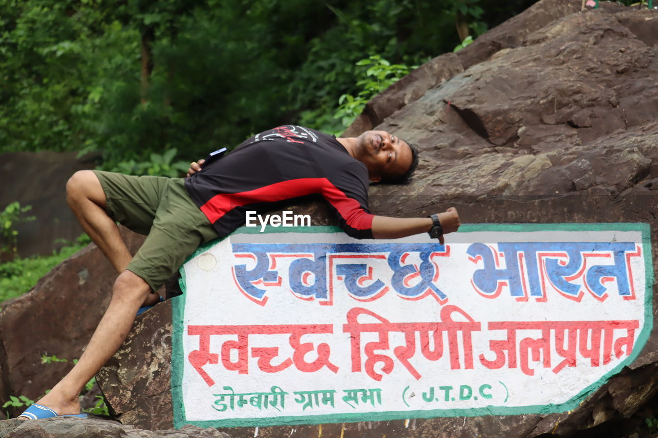 communication, text, sign, one person, adult, rock, nature, western script, men, lifestyles, relaxation, day, outdoors, full length, leisure activity, young adult, casual clothing