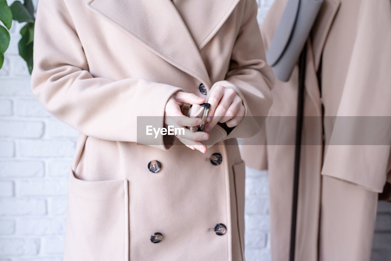 Woman in beige coat standing in front of hanger rack and choosing outfit dressing. selection of 