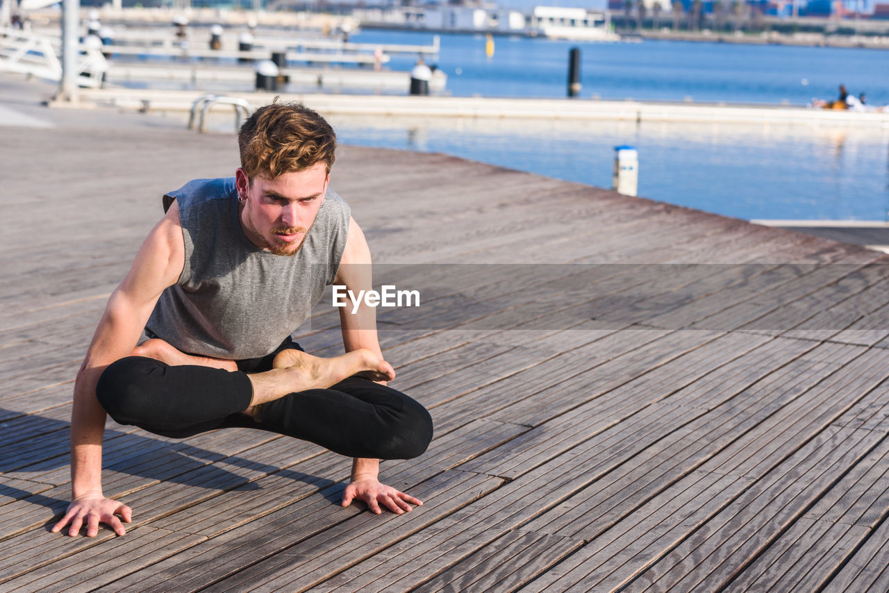 Full length of young man sitting on pier over sea